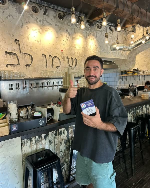 הבעלים של מסעדת שימו לב בתל אביב עומד ליד הבר, מחזיק את כרטיס TapIL ומרים אגודל